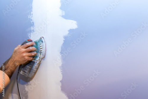 Obraz na plátně Hand using an orbital sander on a wall, preparing surface for paint