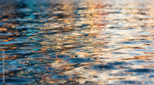 Abstract water ripples with golden sunset reflections on a dark surface
