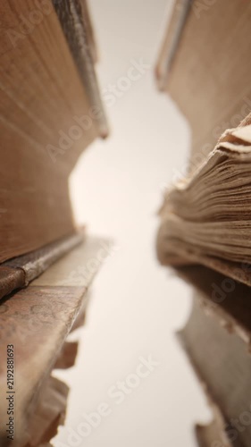 Cinematic slow push-in through stacks of old vintage books, filmed with a probe lens. Detailed close-up perspective of aged book spines and pages creates an atmospheric visual representing education