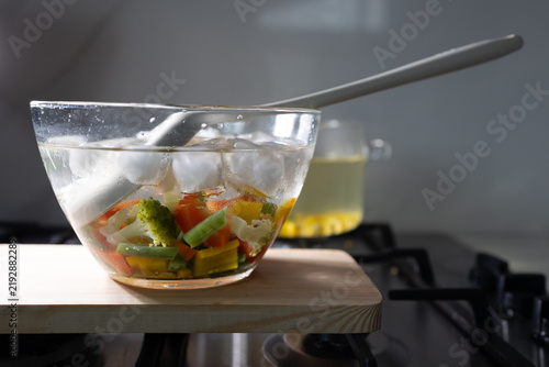 Foto Cooling blanched vegetables in ice water in a glass bowl on a wooden cutting boa