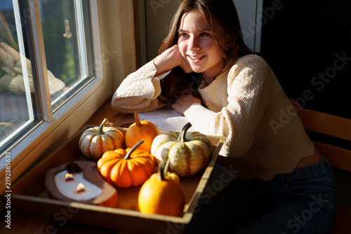 Teen girl relaxing by window with decorative pumpkins at home
