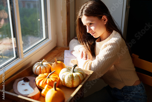 Teen girl relaxing by window with decorative pumpkins at home