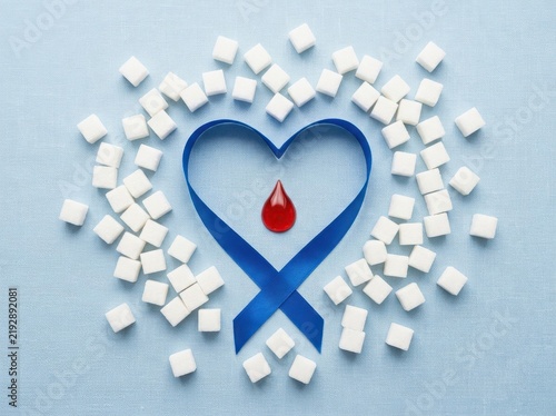 Heart shaped ribbon with blood drop surrounded by sugar cubes on blue background symbolizing diabetes awareness