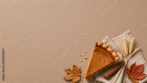 Pumpkin pie slice on beige background, autumn thanksgiving dessert with cinnamon and maple leaves, flat lay copy space