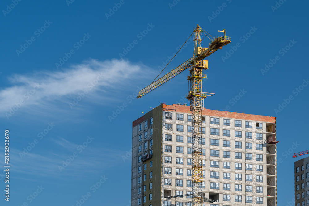 Fototapeta premium Bright blue sky frames an active construction site with crane and rising building in mid-progress