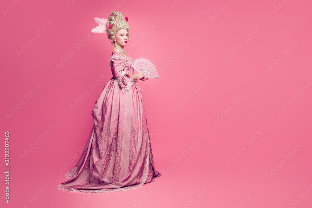 Fototapeta premium Photo of gorgeous wealthy lady in baroque style antique dress enjoying ballroom occasion holding fan isolated pink color background