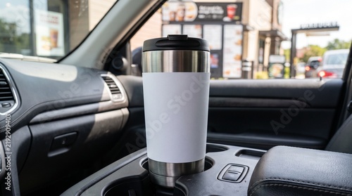 Stainless steel coffee tumbler in vehicle cup holder parked at morning fast food drive thru window