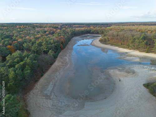 High-angle drone perspective showing the low water level remaining in the Kibbelkoele recreational lake, surrounded by Drenthe forests during its 5-year maintenance drainage