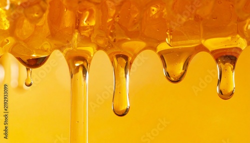 Golden sweet honey dripping from organic honeycomb close-up view, liquid amber nectar flowing in drops against a warm yellow background texture