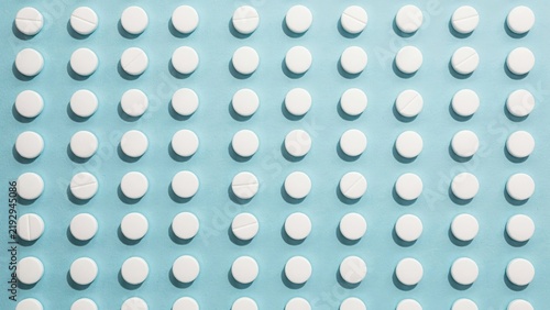 White round pharmaceutical pills arranged in a neat grid pattern on a soft blue background with health care