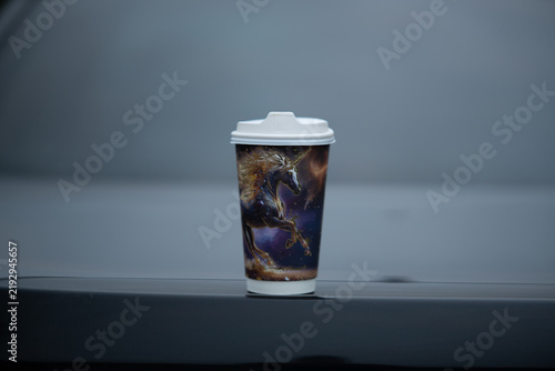 Coffee cup with a unicorn design placed on a car hood in an outdoor setting