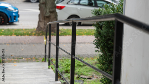 Stairs with a handrail beside a bush near parked cars on a city street