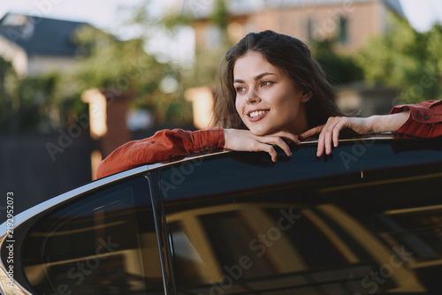 Obraz na plátně Cheerful woman outdoors, leaning on a car, enjoying a sunlit moment, relaxed pos