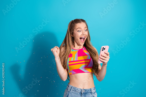Fotografie Joyful teenage girl celebrates great news with a vibrant smile while holding a s