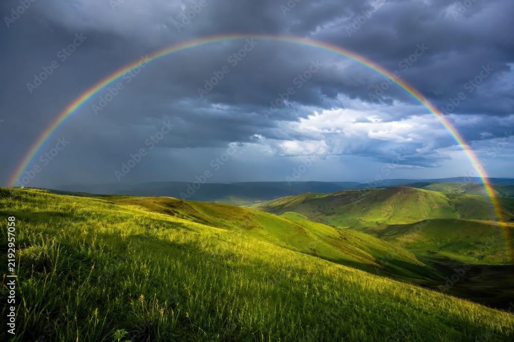 Obraz premium Rainbow arching over wet green rolling hills