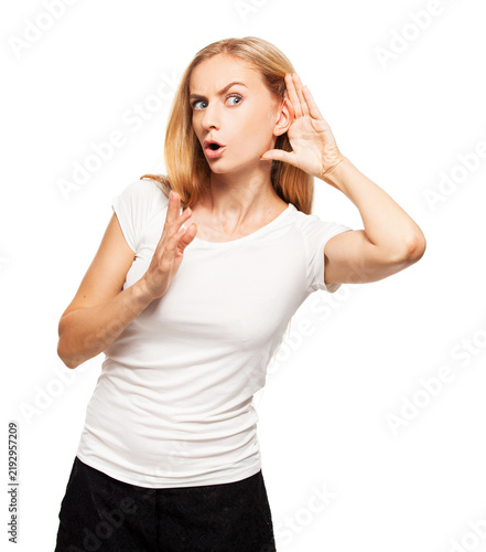 Surprised young woman listening with hand near ear and holding palm up. Blonde girl in white t-shirt eavesdropping on gossip isolated on white background.