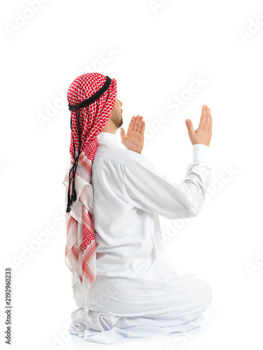 Foto Side view of Muslim Arab man in traditional clothing sitting on knees praying with open hands isolated on white background