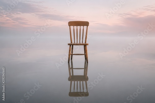 Wooden chair standing alone in shallow lake water at dawn