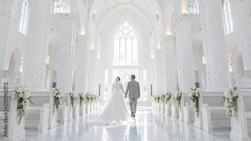 Obraz na płótnie 白いチャペルを手をつないで歩く中高年の新郎新婦の後ろ姿