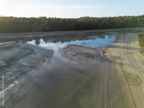 Aerial drone view showing sky reflections in the shallow remaining water and exposed sandbanks of the drained Kibbelkoele recreational lake during maintenance