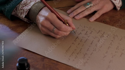 An antique young woman in a resurgent dress, sitting at the table and writing a letter with a vintage pen on an old paper sheet of parchment. The girl is writing a letter in handwritten script. 

