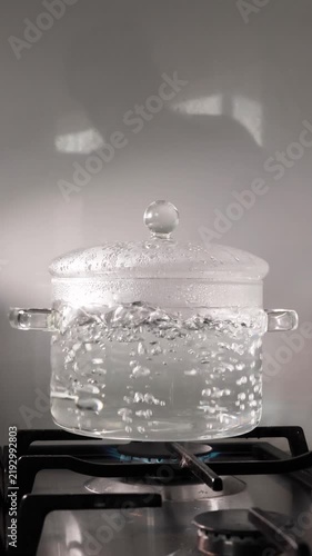Boiling water in a glass pot with a lid on a gas stove