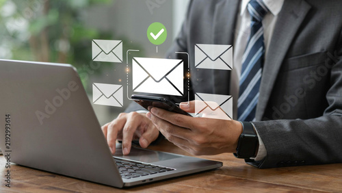 Businessman checking mobile phone with email notifications from laptop during modern office work