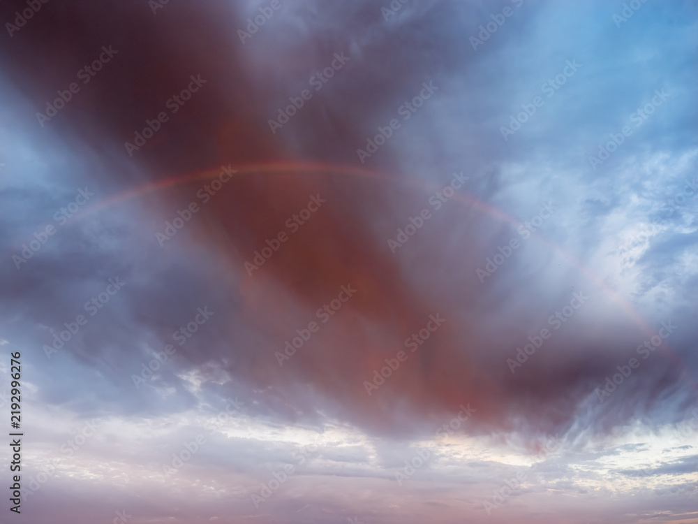 Obraz premium Faint Rainbow Beneath Dramatic Storm Clouds After Rain at Sunrise
