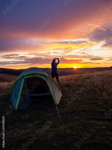 Man Taking Smartphone Photo at Sunset Near Camping Tent
