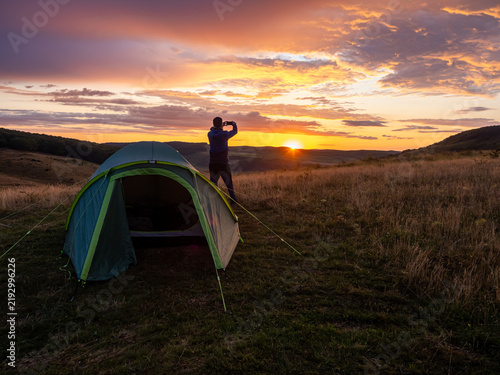 Man Taking Smartphone Photo at Sunset Near Camping Tent