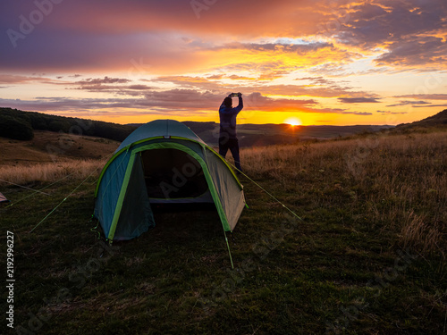 Man Taking Smartphone Photo at Sunset Near Camping Tent