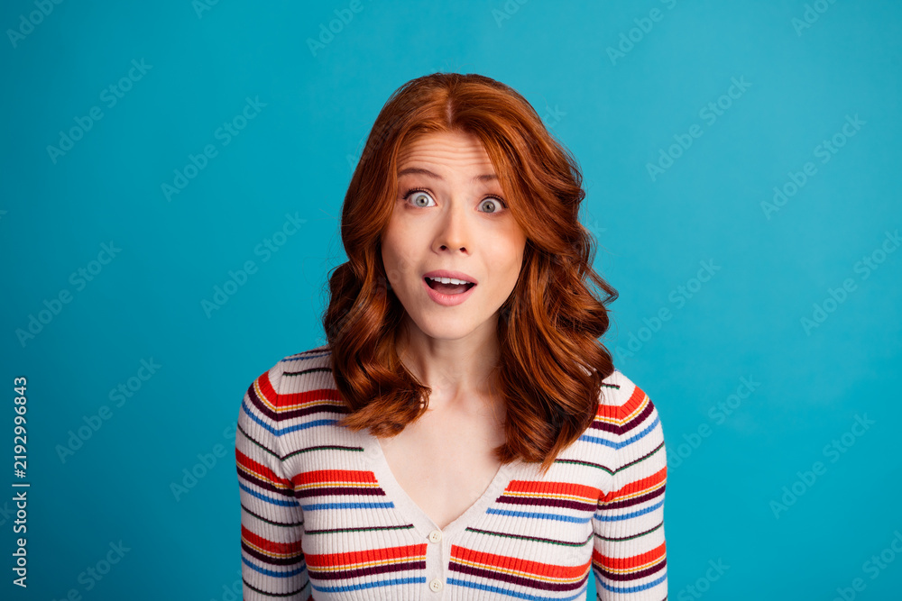 Fototapeta premium Surprised redhead woman with striped sweater looking amazed against a bright blue background