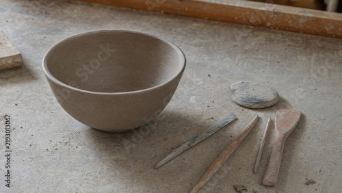 Unfinished Clay Bowl and Wooden Pottery Tools on a Dusty Workbench