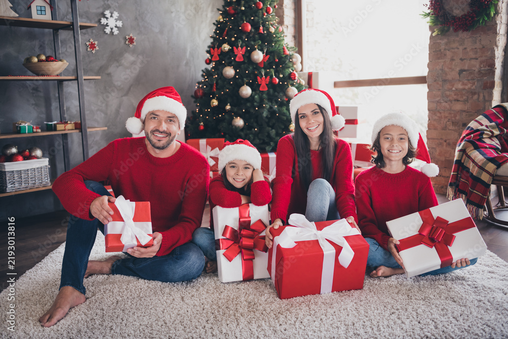 Naklejka premium Happy family in Santa hats opening Christmas gifts by a decorated tree at home on holiday morning