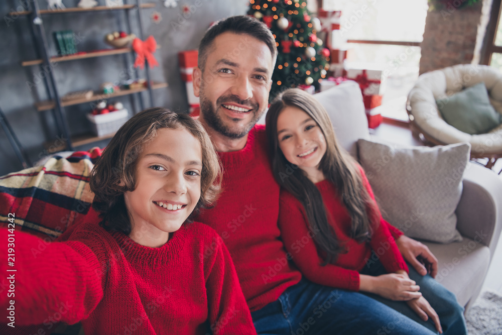 Obraz premium Happy father and children wearing red sweaters taking a Christmas family selfie on a cozy living room couch with tree and gifts