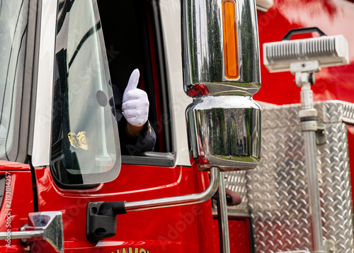 Принти на полотні Firefighter's gloved hand gives a thumbs up from a firetruck window, conveying reassurance, approval, confidence, readiness, and successful emergency response