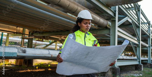 Young mechanical engineer holding blueprint drawing to checking and inspection gas pipeline system new construction project of industrial.