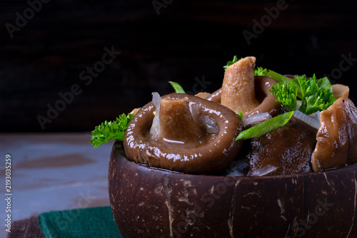 Pickled milk mushrooms with onion and spices topped with parsley in wooden bowl. Russian cuisine appetizer. Close-up