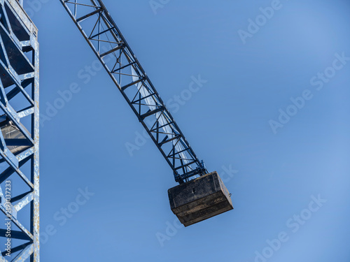 Foto The heavy concrete counterweight of a tower crane hangs from its lattice jib, isolated against an unbroken blue sky
