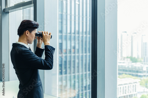 Foto Businessman Using Binoculars to Look at City Skyline from Office Window