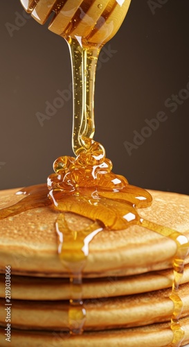 Pouring golden honey on a stack of pancakes in a close-up food photography with warm background and natural texture