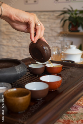 Tea ceremony scene with a hand pouring hot tea from a clay pot into a row of ceramic cups on a wooden tray, capturing calm focus and traditional tea ritual.