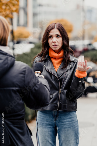 Photography Woman giving a street interview in a leather jacket and orange turtleneck, gestu