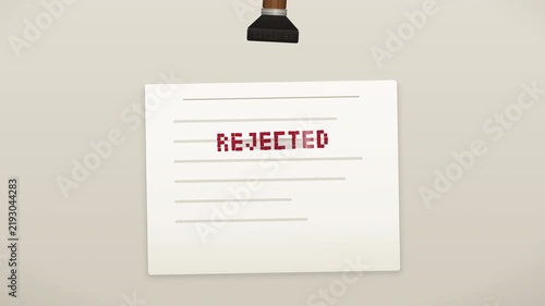 A wooden-handled rubber stamp presses down onto a paper document, compressing it on impact and leaving a bold red 
