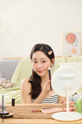 Foto Young woman applying makeup with a brush at a vanity table in a cozy bright room