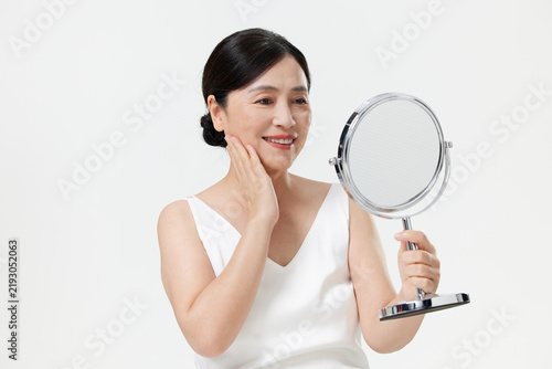 Foto Happy mature Asian woman looking in a mirror and touching her face