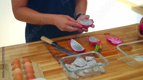 Man preparing dragon fruit for meal prep, peeling sliced pitaya over wooden cutting board with cubed pieces in glass container