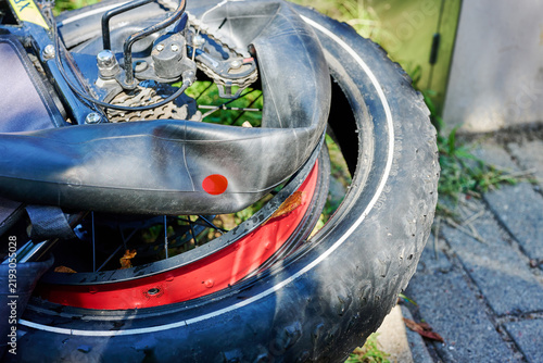 A bicycle with a damaged tire leans on a wall in an urban area on a sunny day. Parts of the bike show signs of wear
