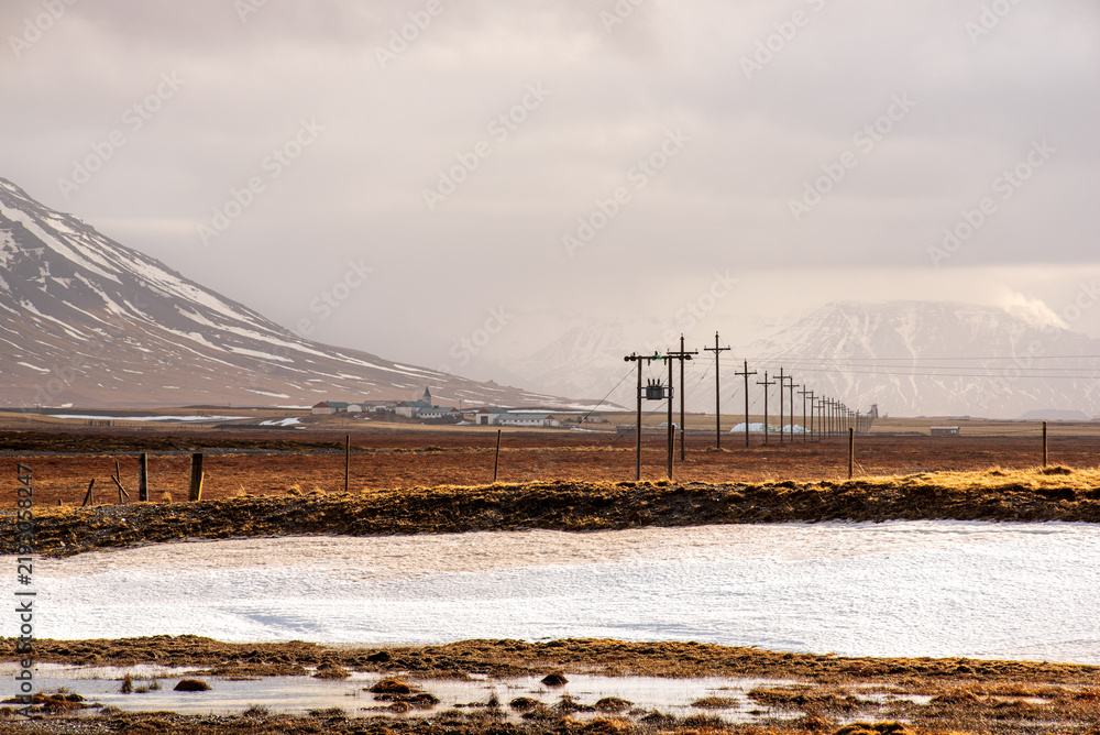 Fototapeta premium Icelandic rural landscape with utility poles and snowy mountains
