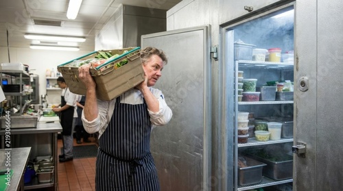 Chef carrying produce crate into commercial kitchen walk in refrigerator